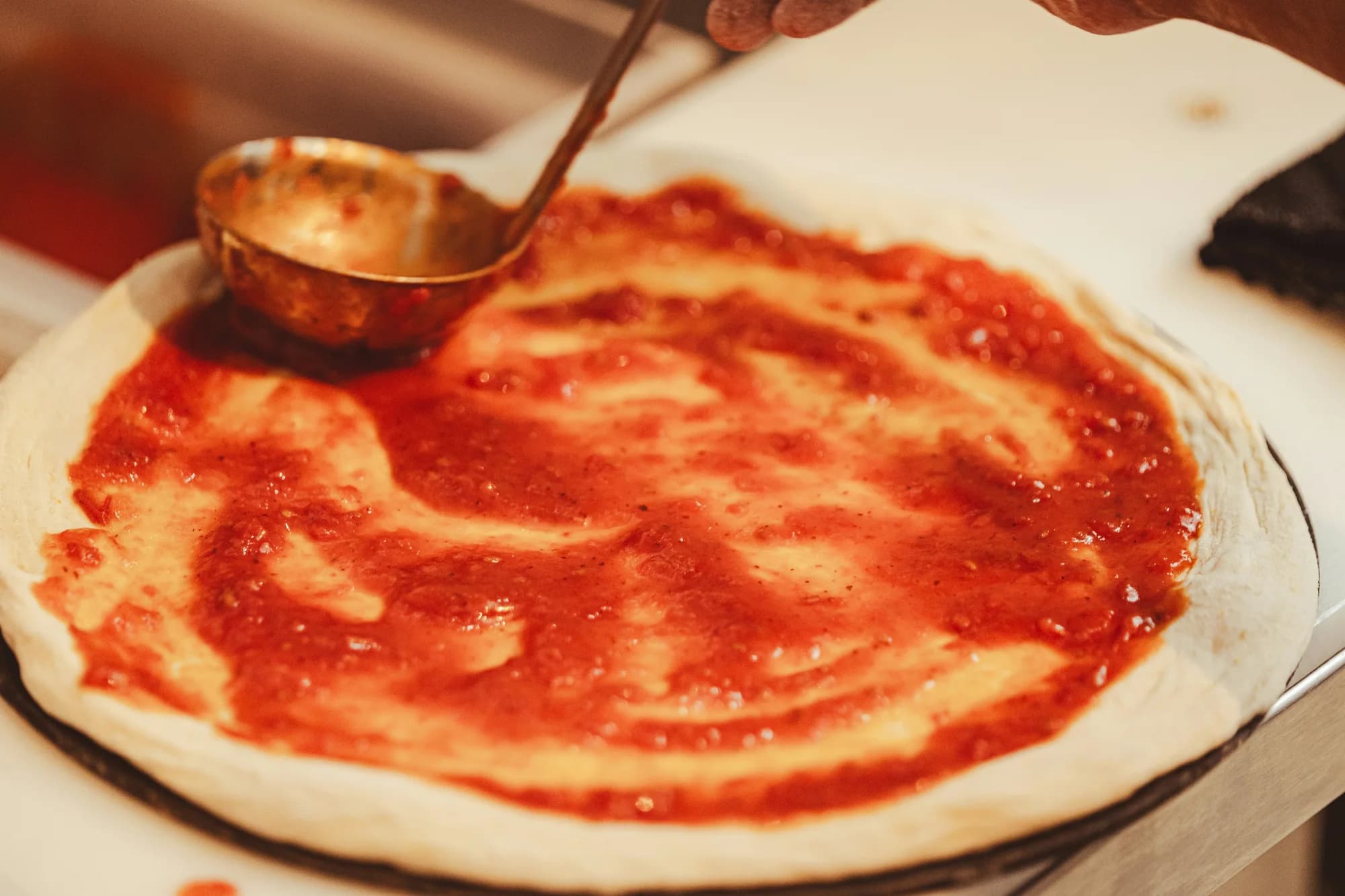 Pizza sauce being spread on dough — representative photo, not taken at Paesano Pizza — Miller Street