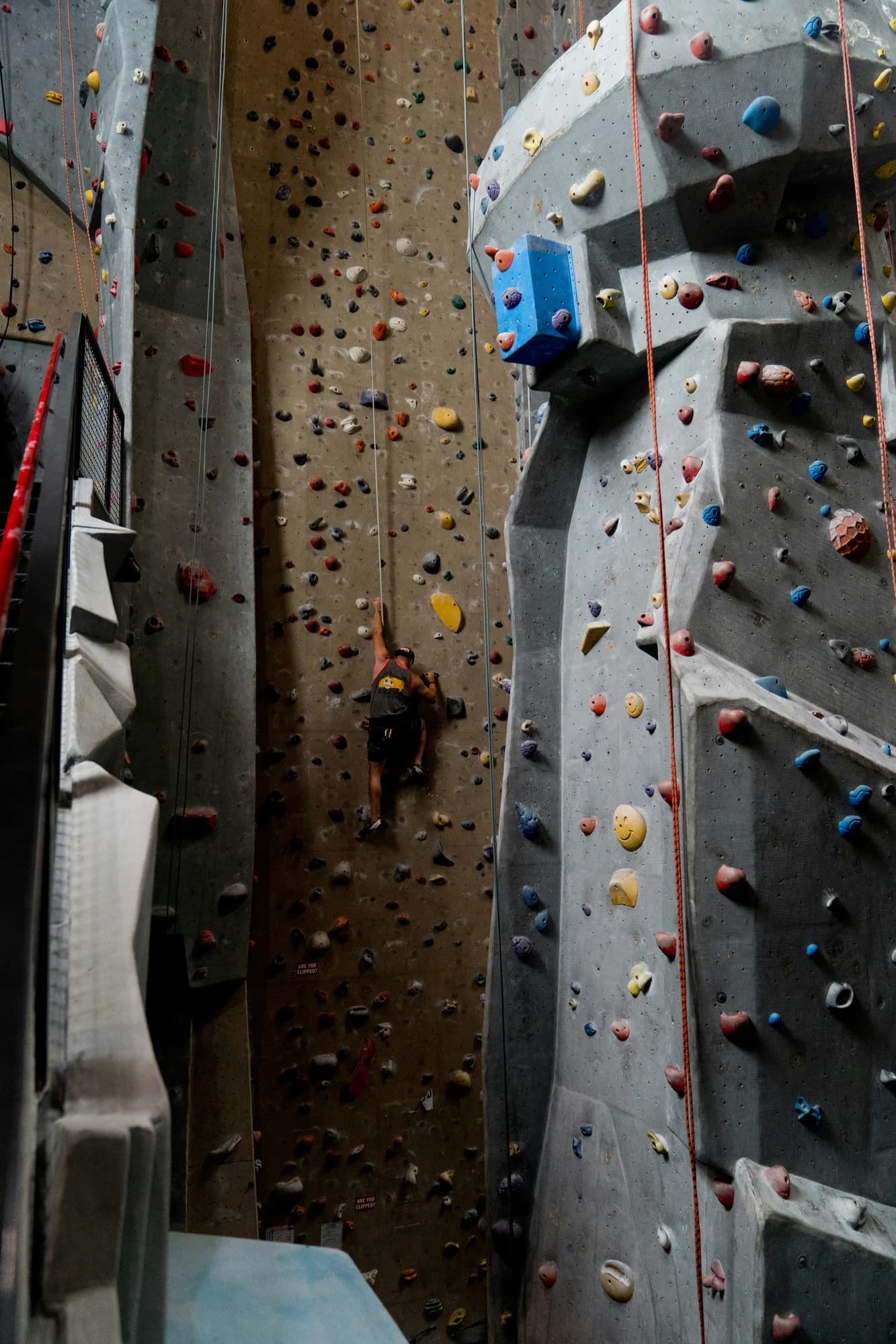 A person climbing a tall indoor rock climbing wall. — representative photo, not taken at The Climbing Academy — The Prop Store